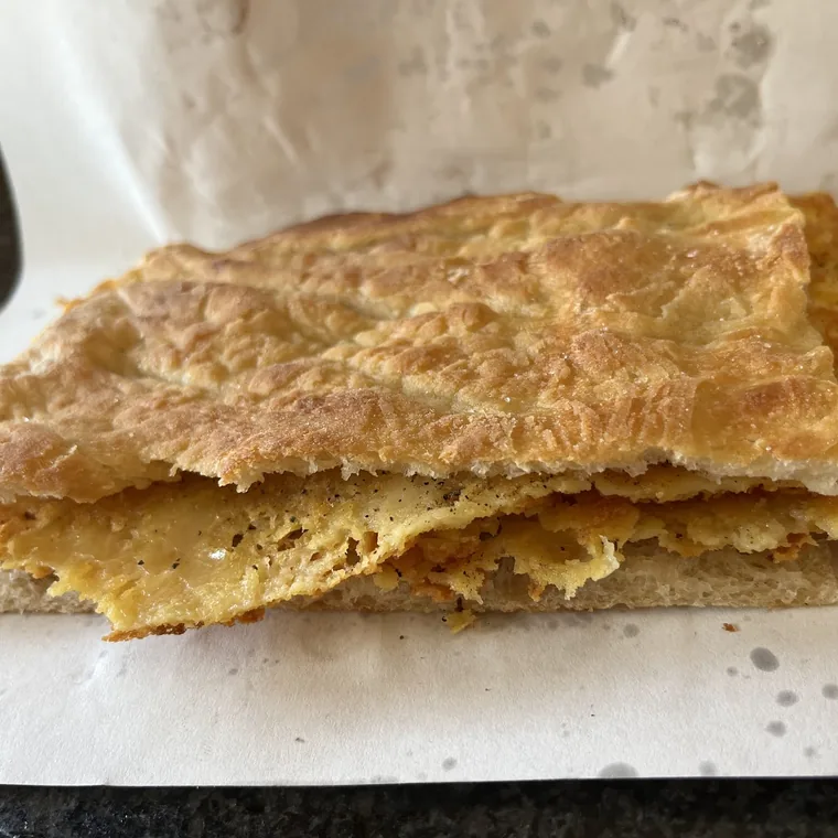 Un pezzo di focaccia aperto a metà e riempito di cecina dorata, appoggiato sulla carta da banco.