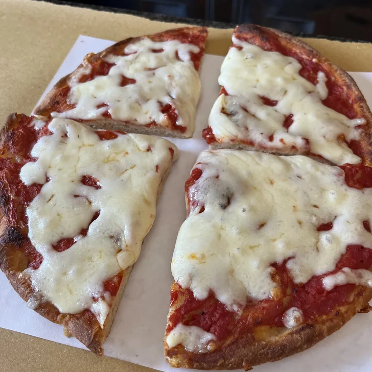 Una pizza margherita tonda tagliata in quattro spicchi, appoggiata sul cartone aperto.