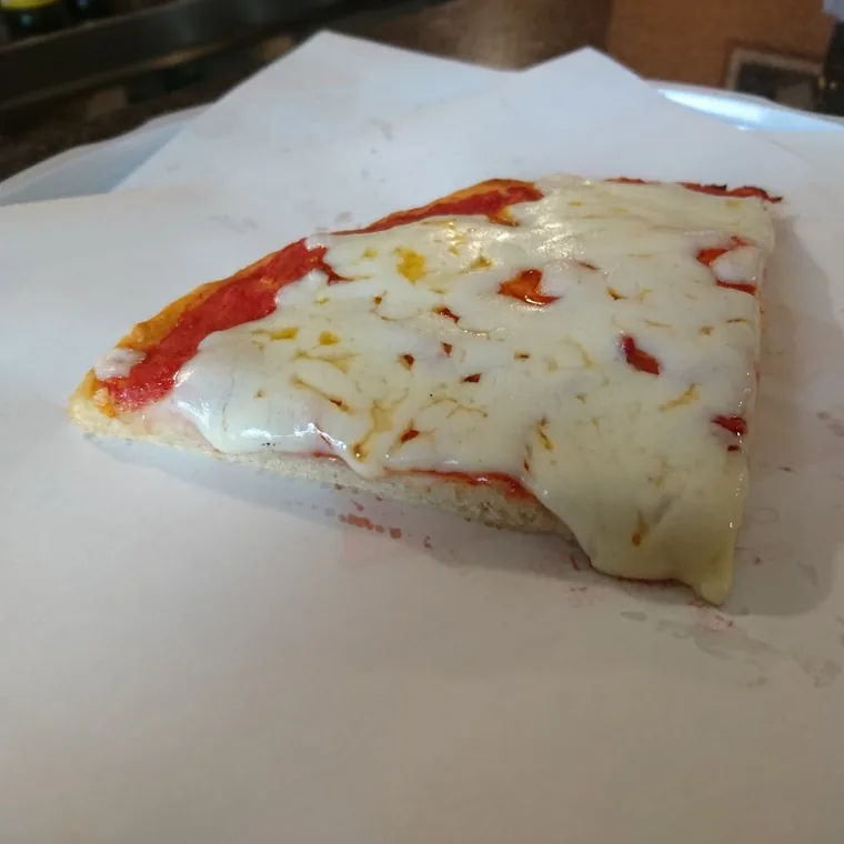 Un trancio quadrato di pizza margherita con la mozzarella ancora lucida, servito sulla carta.